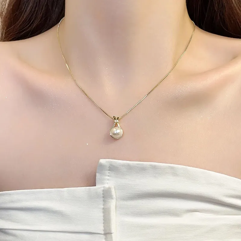 Gold necklace with a pear-shaped pearl pendant, resting gracefully on the neckline.