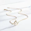 Gold necklace with a pear-shaped pearl pendant encased in a delicate gold setting, adorned with a small crystal accent.