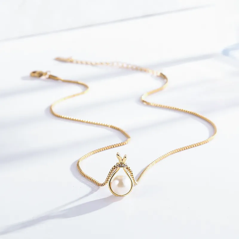 Gold necklace with a pear-shaped pearl pendant encased in a delicate gold setting, adorned with a small crystal accent.