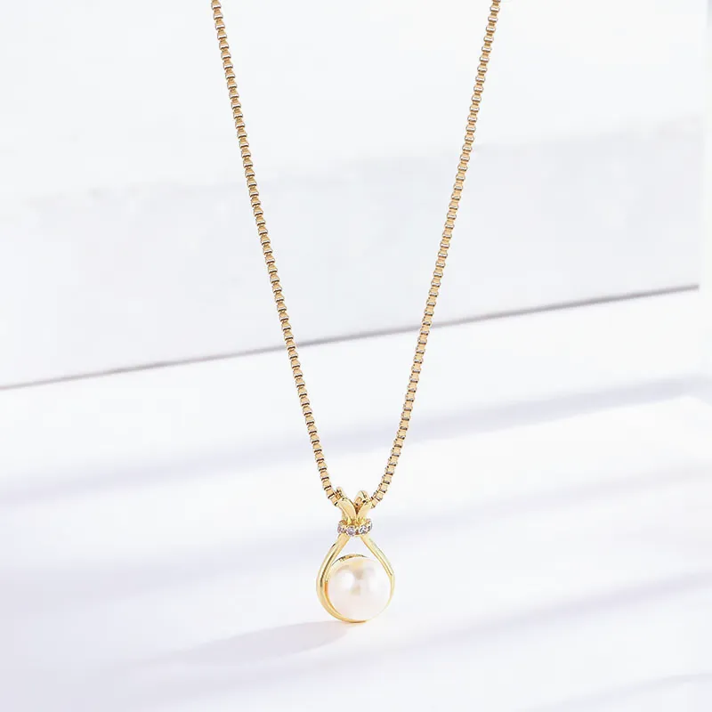 Gold necklace with a pear-shaped pearl pendant, highlighted by small sparkling stones around the pearl, resting on a smooth gold chain.