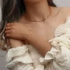 Model wearing an 18K gold-plated heart chain jewelry set, including a choker necklace, bracelet, and rings, styled with a romantic off-shoulder white dress.