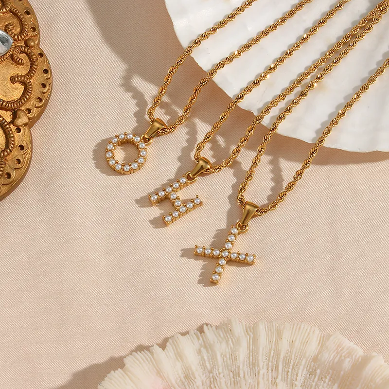 A set of gold-plated alphabet necklaces with pearls in the shapes of O, H and X, hanging on twisted gold chains.