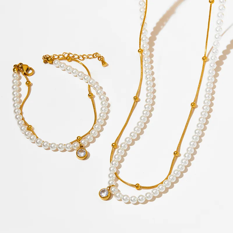 A matching 18K gold-plated pearl necklace and bracelet set with crystal pendants, displayed on a white background for a sophisticated presentation.