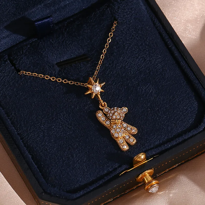 A gold teddy bear pendant necklace, with the bear and star charm both decorated with cubic zirconia crystals, placed inside a jewelry box.