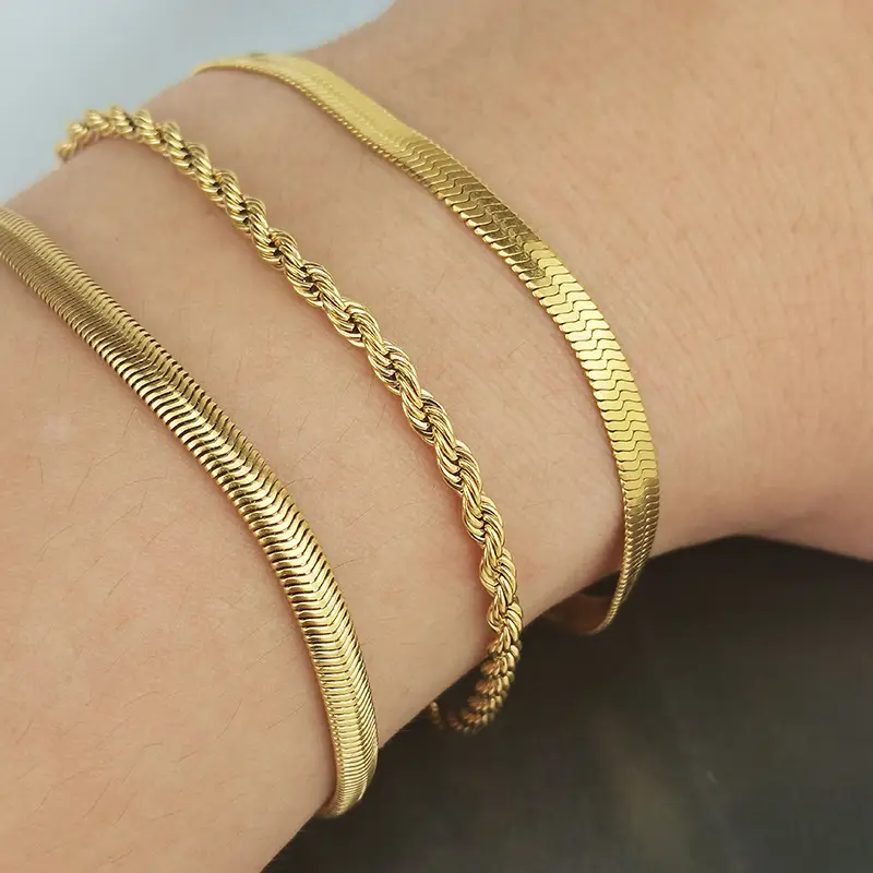 A set of gold bracelets, featuring two herringbone chains and one twisted rope chain, elegantly worn on a wrist.