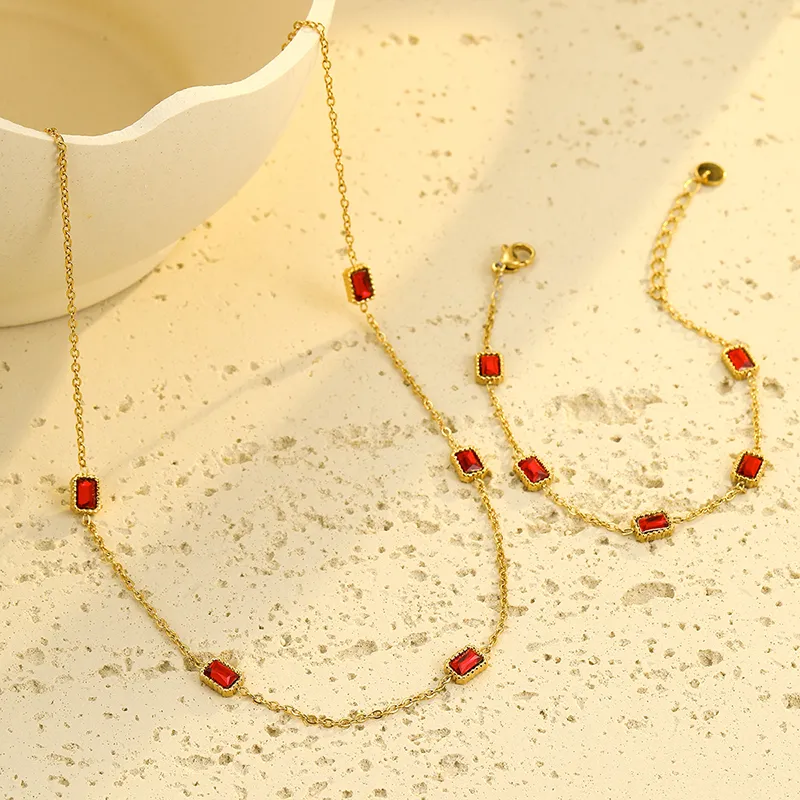 Gold necklace and bracelet set featuring rectangular red cubic zirconia stones, placed elegantly in a gold chain design.