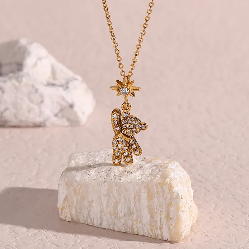 Gold teddy bear pendant necklace with cubic zirconia stones and a star charm, displayed on a smooth stone surface.