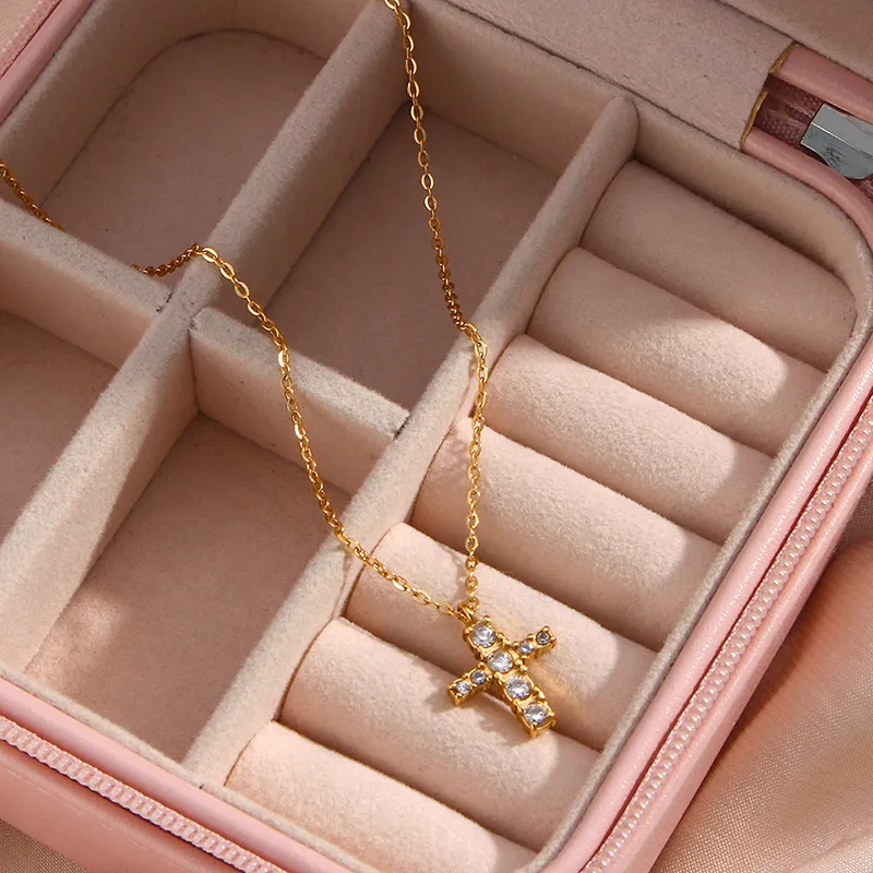 Gold cross necklace with cubic zirconia crystals lying in a jewelry box with soft compartments, showcasing the pendant and fine gold chain.