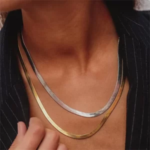 A layered gold and silver herringbone chain necklace set, elegantly worn over a black pinstripe blazer for a sophisticated look.