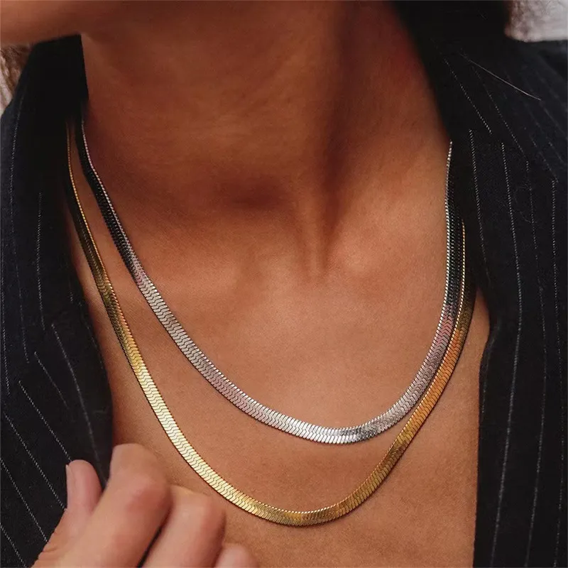 A layered gold and silver herringbone chain necklace set, elegantly worn over a black pinstripe blazer for a sophisticated look.