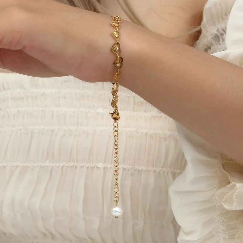 Close-up of a model wearing an 18K gold-plated heart chain bracelet with an adjustable extension and a pearl charm, styled with a white ruffled blouse.