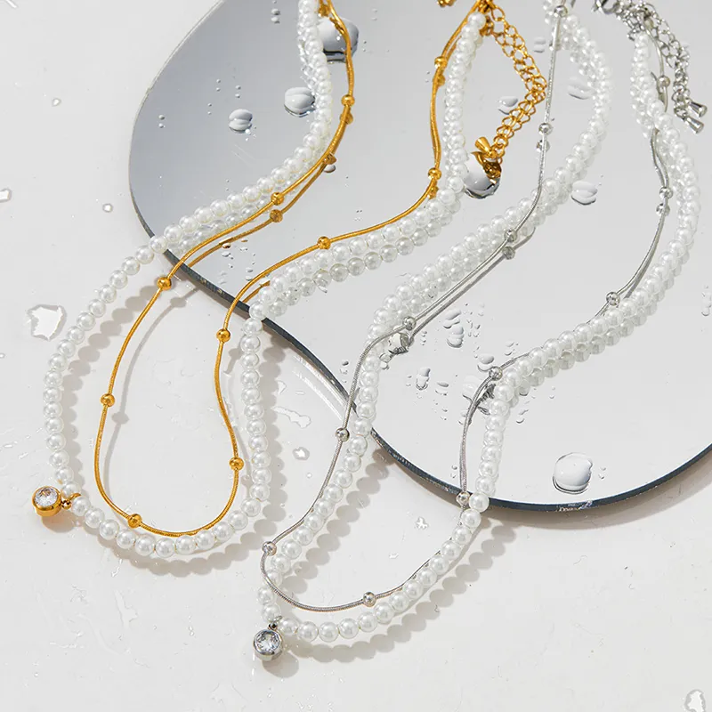 18K gold and silver-plated pearl necklaces with crystal pendants, displayed on a reflective surface with water droplets for an elegant and chic aesthetic.