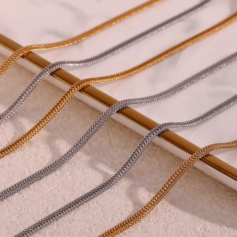 A close-up of gold and silver herringbone chains elegantly displayed on a marble surface, showcasing their smooth and reflective design.