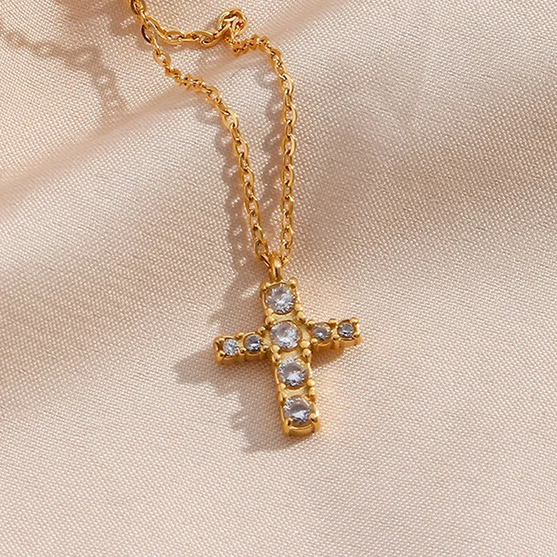 Gold cross necklace adorned with cubic zirconia crystals, suspended from a fine gold chain.
