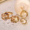 A set of 18K gold-plated rings with marquise-cut cubic zirconia in different colors, displayed on a wet reflective surface to emphasize their waterproof and tarnish-resistant qualities.