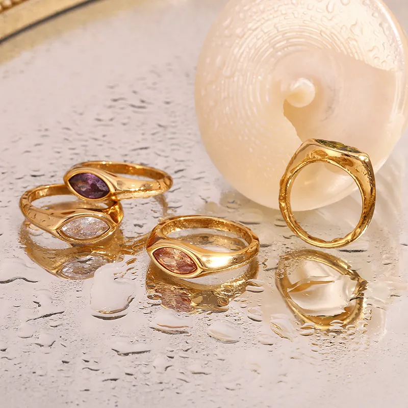 A set of 18K gold-plated rings with marquise-cut cubic zirconia in different colors, displayed on a wet reflective surface to emphasize their waterproof and tarnish-resistant qualities.