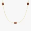 Close-up of a gold necklace featuring three red cubic zirconia stones set in rectangular shapes, linked by a delicate chain.