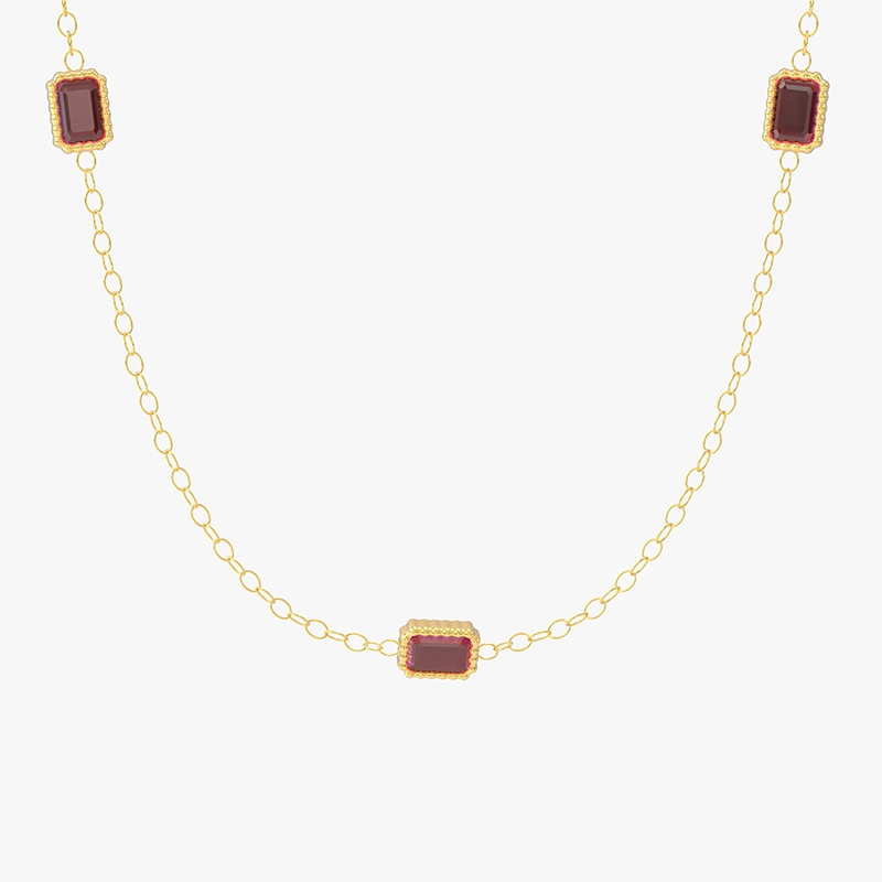 Close-up of a gold necklace featuring three red cubic zirconia stones set in rectangular shapes, linked by a delicate chain.