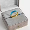 A gold-plated ring with a blue marbled enamel inlay, elegantly displayed in a gray velvet jewelry box, highlighting its modern and sophisticated design.
