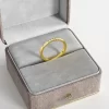 A thin 18K gold ring with 10 cubic zirconia stones, displayed in a gray velvet jewelry box, highlighting its delicate and elegant design.