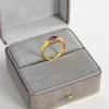 An 18K gold-plated ring with a marquise-cut purple cubic zirconia gemstone, displayed in a gray velvet jewelry box for an elegant presentation.