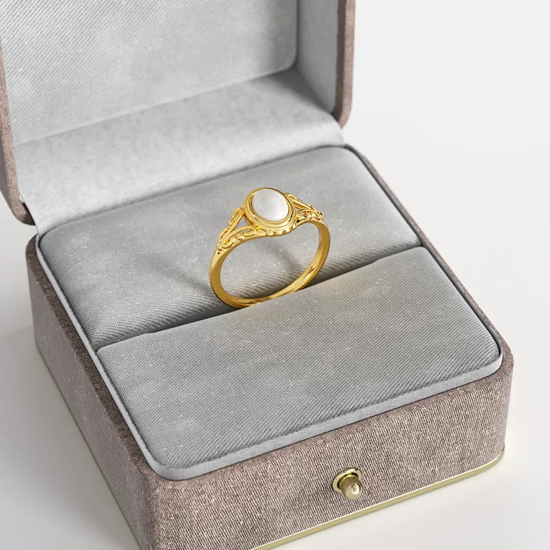 A vintage-style 18K gold-plated filigree ring with a white pearl, elegantly displayed in a gray velvet jewelry box, showcasing its intricate detailing and timeless appeal.